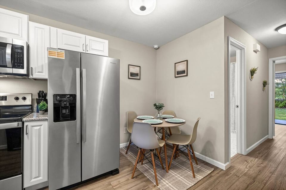 Modern kitchen with dining space — sleek fridge, cozy table for four, and bright hallway view