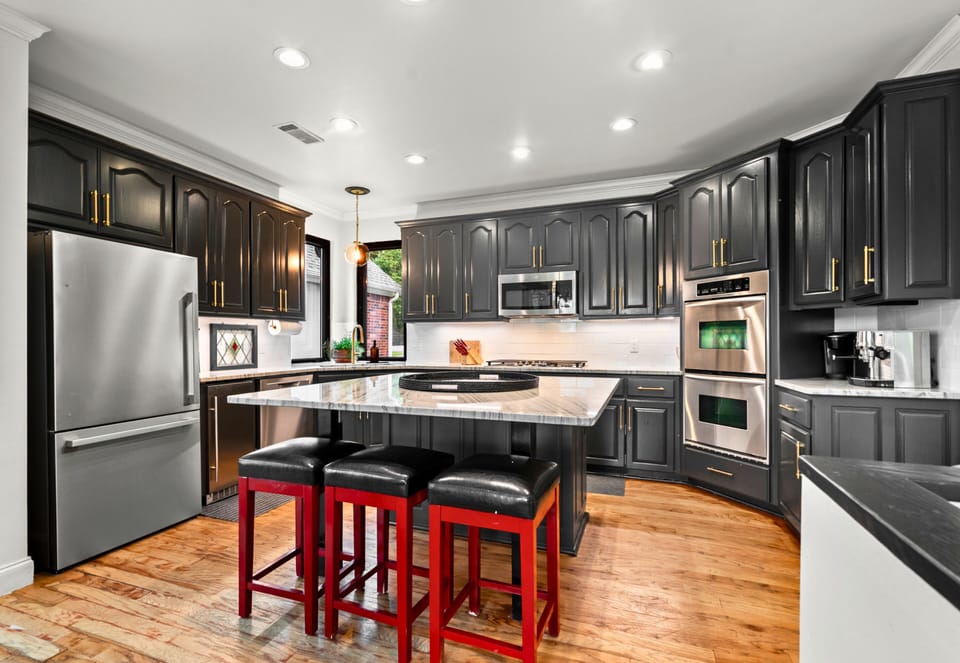 Sleek black cabinetry, gold hardware, and pops of red bring high contrast and bold personality to this stylish chef-ready kitchen.