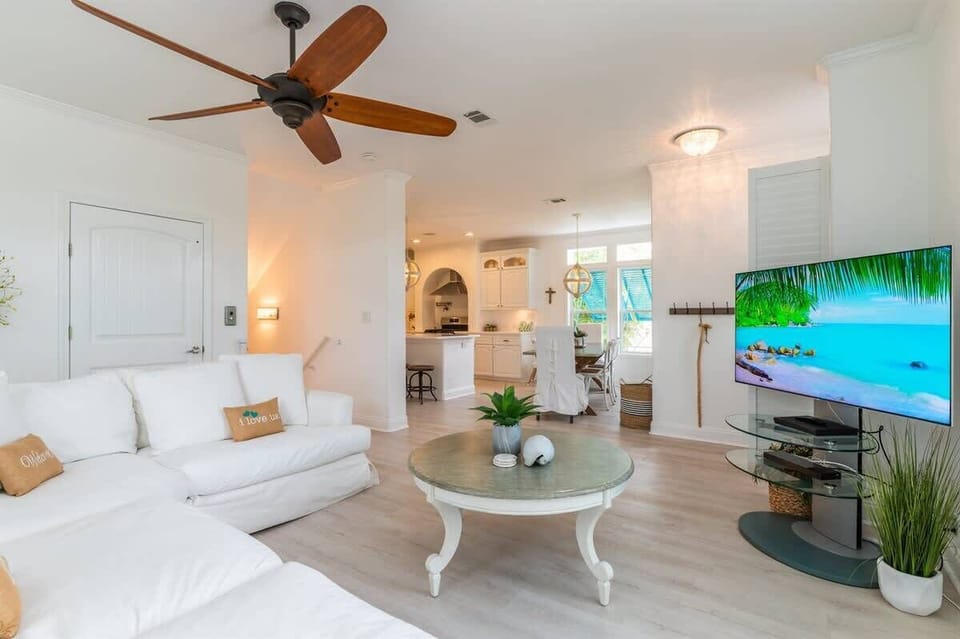 An open living area with a sectional sofa, ceiling fan, and smart TV flows into a dining space and full kitchen.