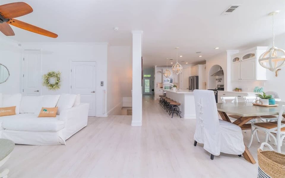 An open living area with a sectional sofa, ceiling fan, and smart TV flows into a dining space and full kitchen.