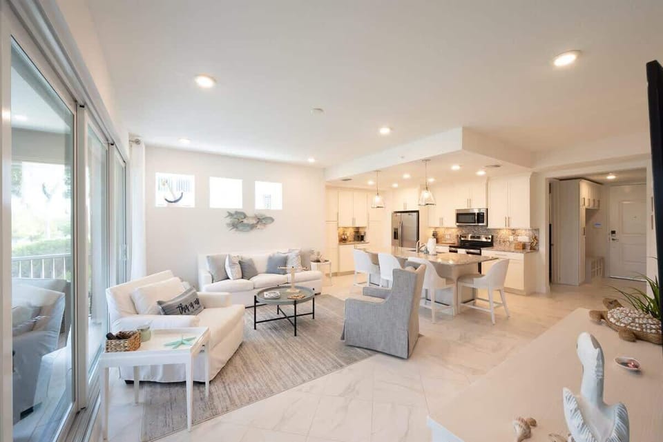 Living space with coastal décor, plush seating, smart TV, and sliding doors to a breezy porch. This open-concept room flows seamlessly into the kitchen and dining areas.