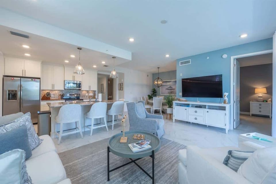 Living space with coastal décor, plush seating, smart TV, and sliding doors to a breezy porch. This open-concept room flows seamlessly into the kitchen and dining areas.