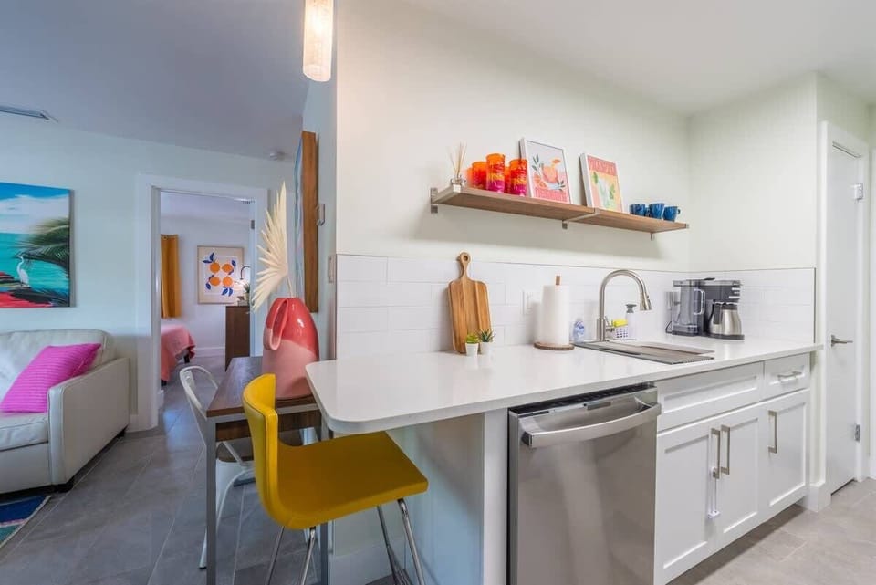 Kitchen with white cabinetry, stainless steel appliances, and quartz counters. Includes a breakfast bar with bright stools, open shelving, and vibrant decor that connects seamlessly to the living area.