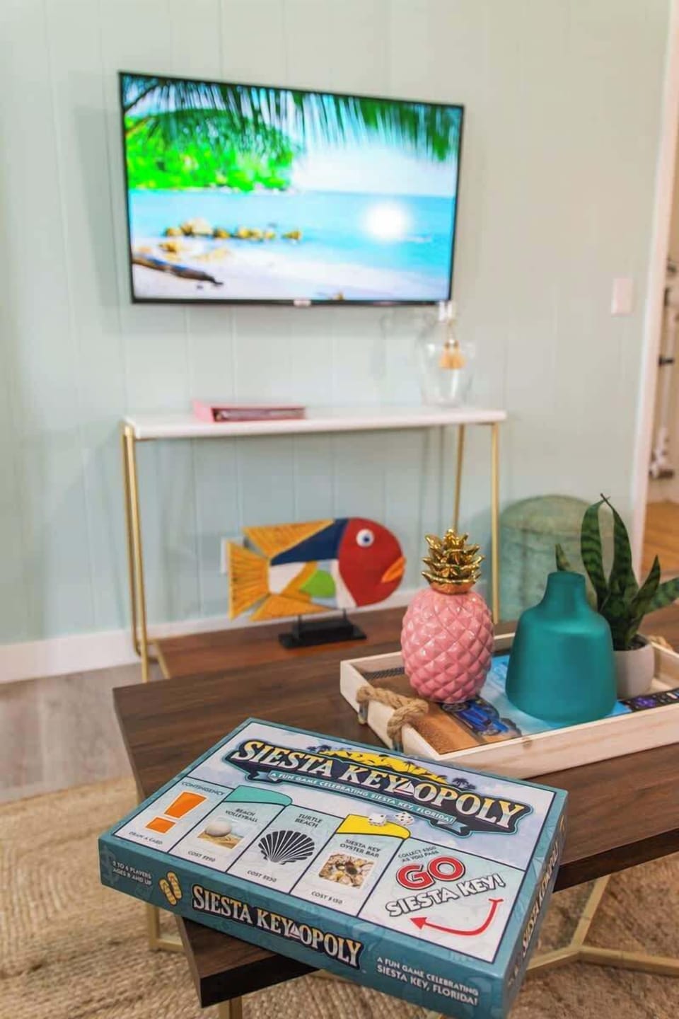 Tropical living room with leather seating, rattan accents, a smart TV, ceiling fan, bright decor, and open layout to the kitchen and dining area.