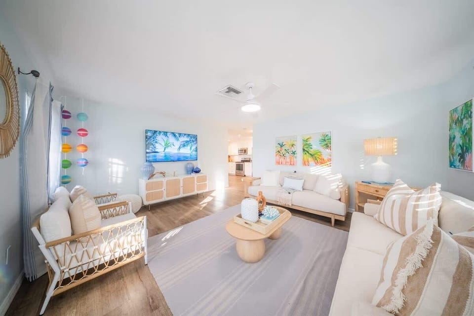 Spacious living area with sofas, rattan chairs, a large smart TV, modern coastal décor, and ceiling fan.