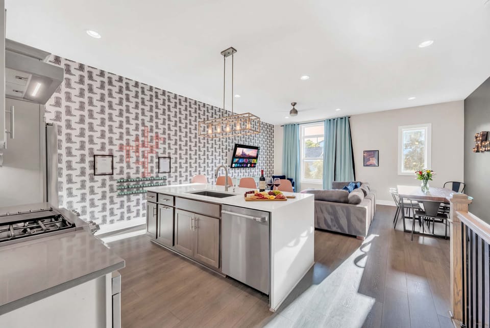 Open-concept kitchen and living area with boot-motif wall art, island seating, sectional, and dining table all visible at once, perfect for planning your day together