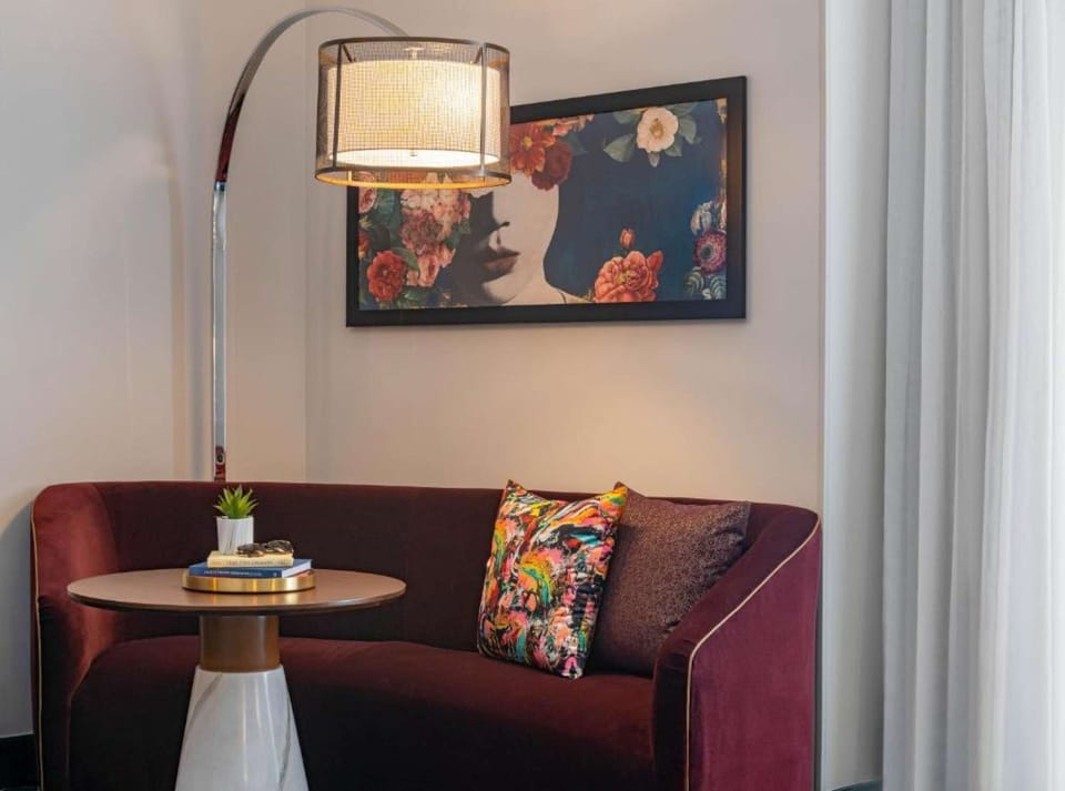 Red velvet loveseat with art and floor lamp in the corner.