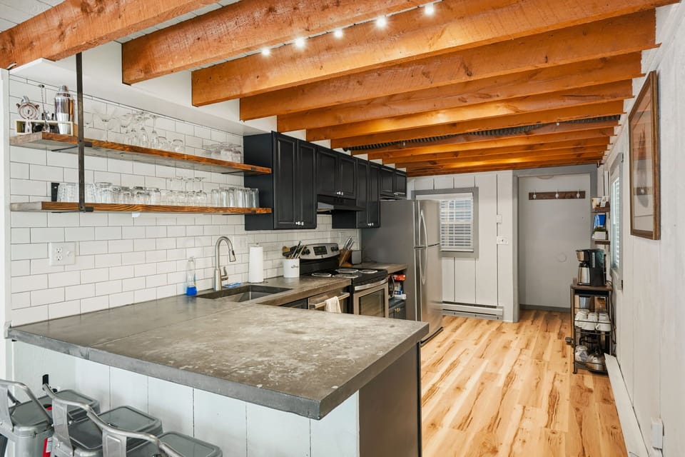 Kitchen with island bar seating, subway tile, dark cabinets, and exposed wood beams