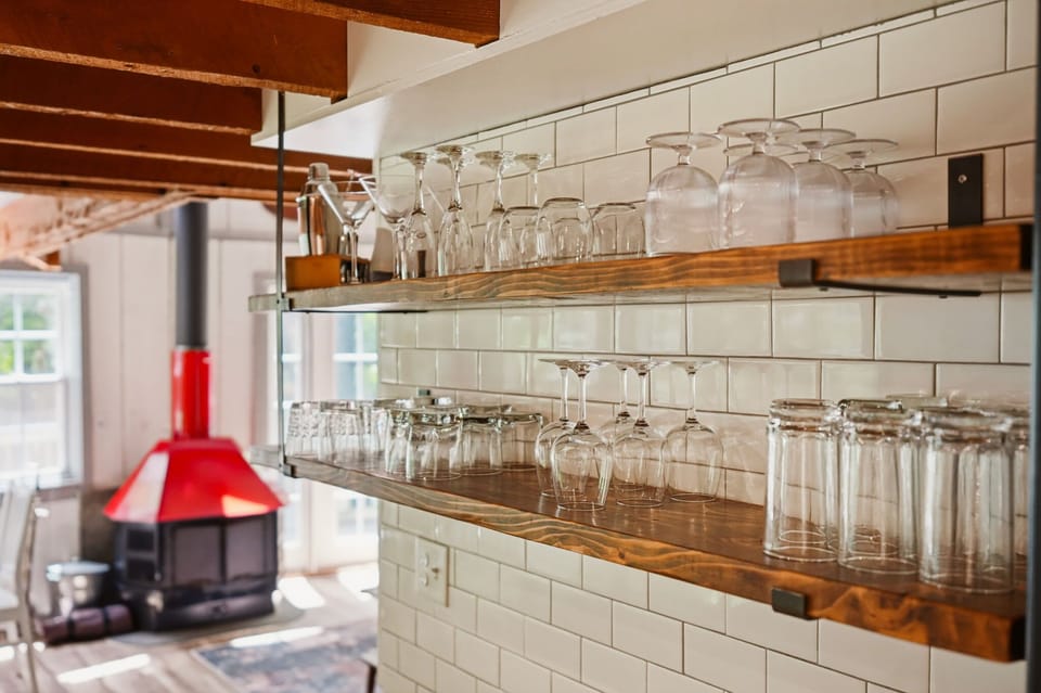 Unique kitchen nook with red wood stove and suspended wine glass rack over subway tile