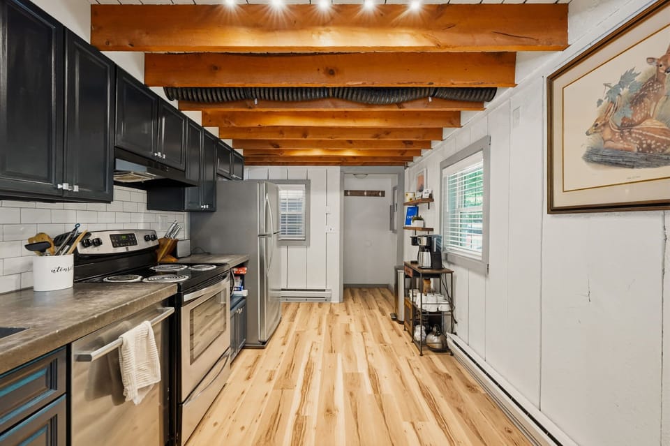 Modern kitchen with dark navy cabinets, exposed beam ceiling, and stainless appliances