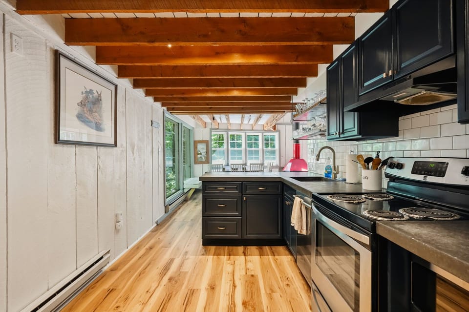 Long kitchen with dark cabinetry, hardwood floors, and sun-filled windows