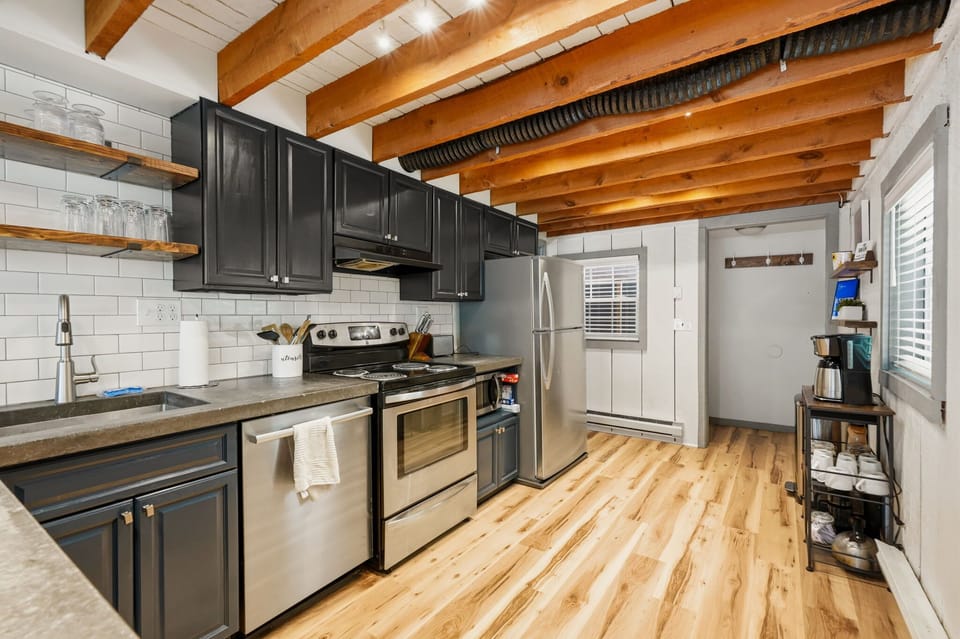 Full kitchen with subway tile backsplash, dark cabinets, and exposed rustic beams