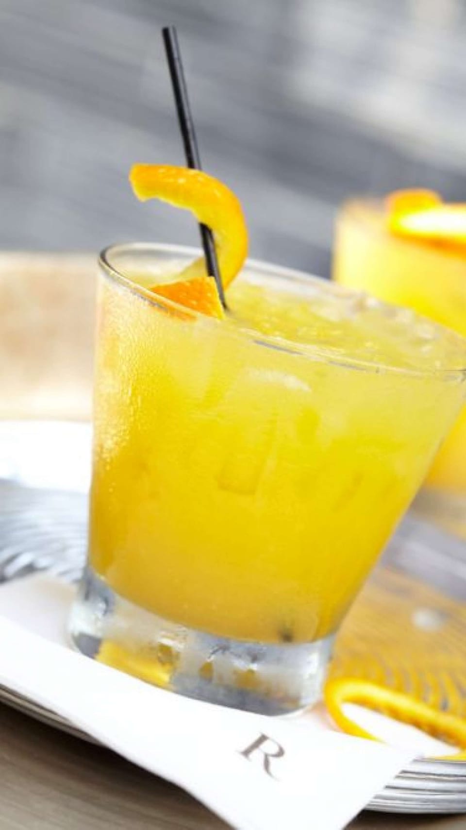 Chilled orange cocktail with a straw and garnish.
