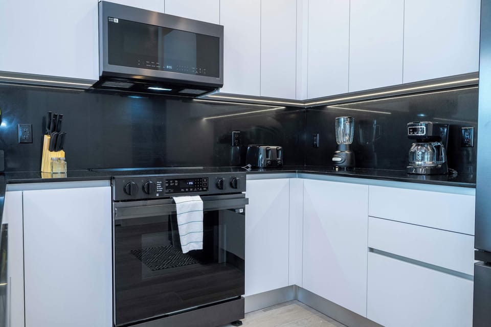Sip coffee at the bar stools in this bright kitchen showcasing white cabinets, black accents, and under-cabinet LED.
