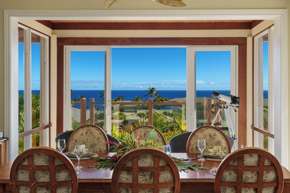 Dining area with ocean view, tropical plants, and telescope by window
