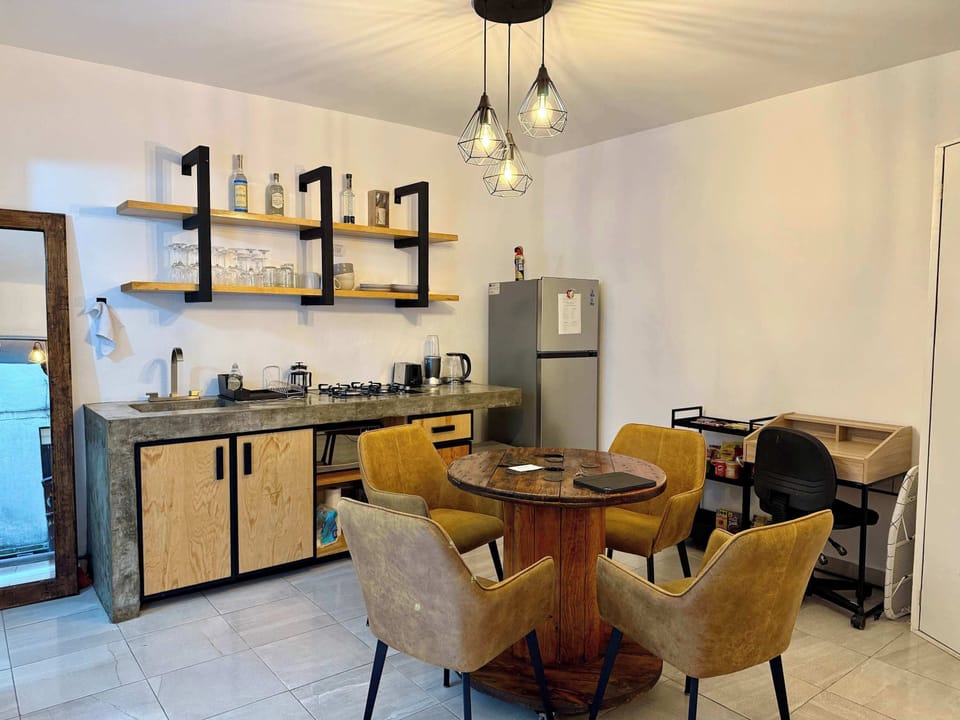 Sala (mesa con 4 sillas, escritorio individual con silla, lámpara de lectura, cocina integrada, espejo alto, clóset, barra con estufa integrada, tarja, repisas con tazas, copas y licores, refrigerador, stand con snacks, minibar)