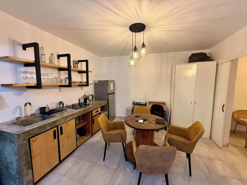 Sala (mesa con 4 sillas, escritorio individual con silla, lámpara de lectura, cocina integrada, espejo alto, clóset, barra con estufa integrada, tarja, repisas con tazas, copas y licores, refrigerador, stand con snacks, minibar)
