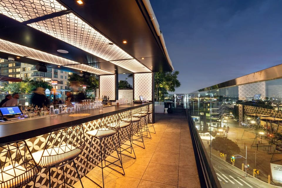 Sip skyline cocktails beneath glowing lights on the rooftop.