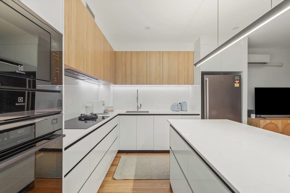 Prepare meals in the modern kitchen, equipped with both gas and induction stovetops, dan oven, a full-size fridge, and minimalist cabinetry offering generous storage—all under stylish ambient lighting.