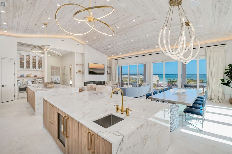 Picture yourself preparing meals in this bright, open kitchen with marble countertops, gold fixtures, and stunning ocean views just beyond the dining area—perfect for entertaining or relaxing after a day at the beach.