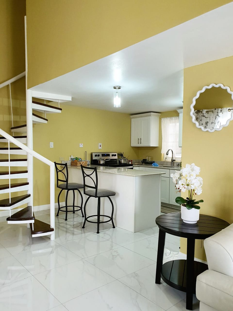 Open kitchen w/ breakfast bar seating & staircase nearby in a bright, airy layout.