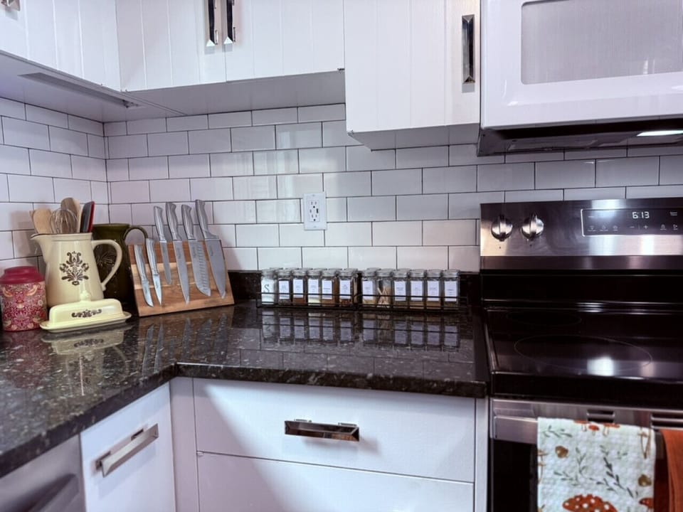 Prepare dinner in this stocked kitchen including spices, prep tools, dishes, pans, and flatware.