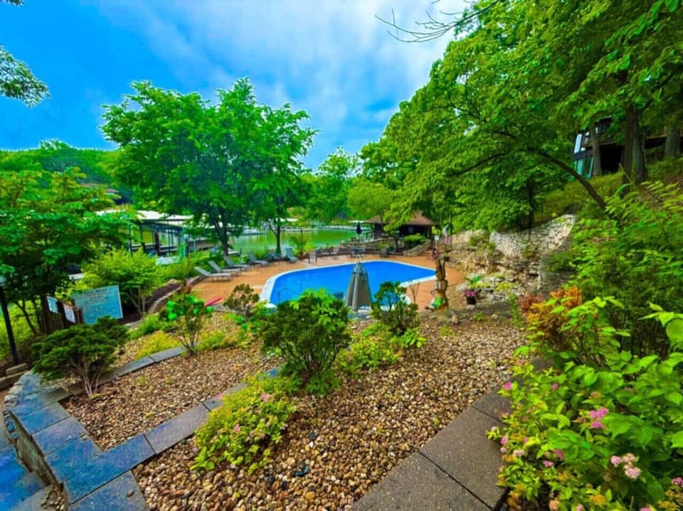 2nd pool with the inviting deck, adorned with shaded seating and lounge chairs, offers the perfect spot to unwind. Beyond the pool, enjoy scenic views of a tranquil waterfront, complete with boat docks and lush landscapes.