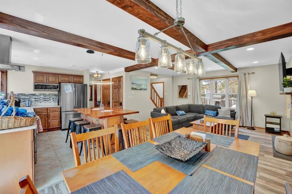 View from the dining table looking into the open-concept living area and modern kitchen. The space features a cozy seating area with a fireplace and TV, a central island with bar seating, and a seamless layout for gathering and entertaining.