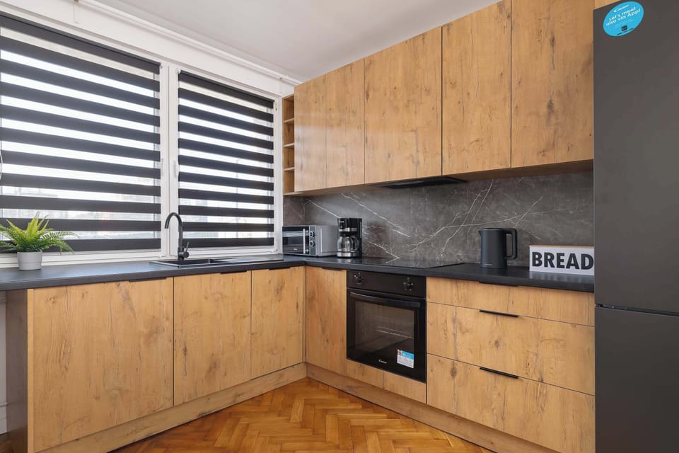 A modern kitchen with wooden cabinets and black countertops. The kitchen includes a built-in oven and stove with a vent hood.
