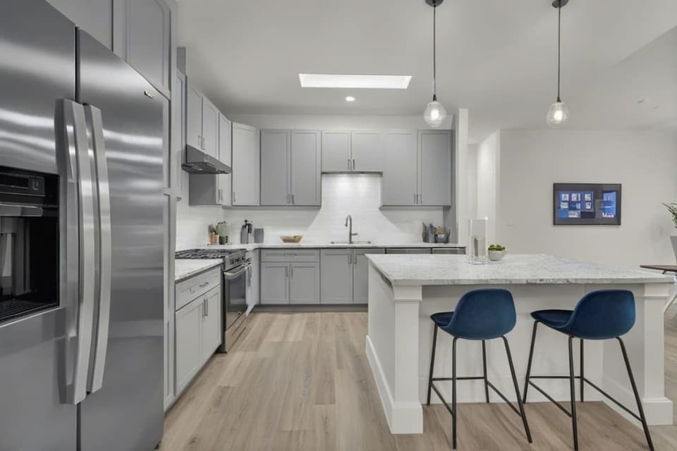 A sleek, modern kitchen with stainless steel appliances, ample counter space, and a spacious island with bar seating. Perfect for cooking, dining, or enjoying a casual coffee in a bright and stylish setting.