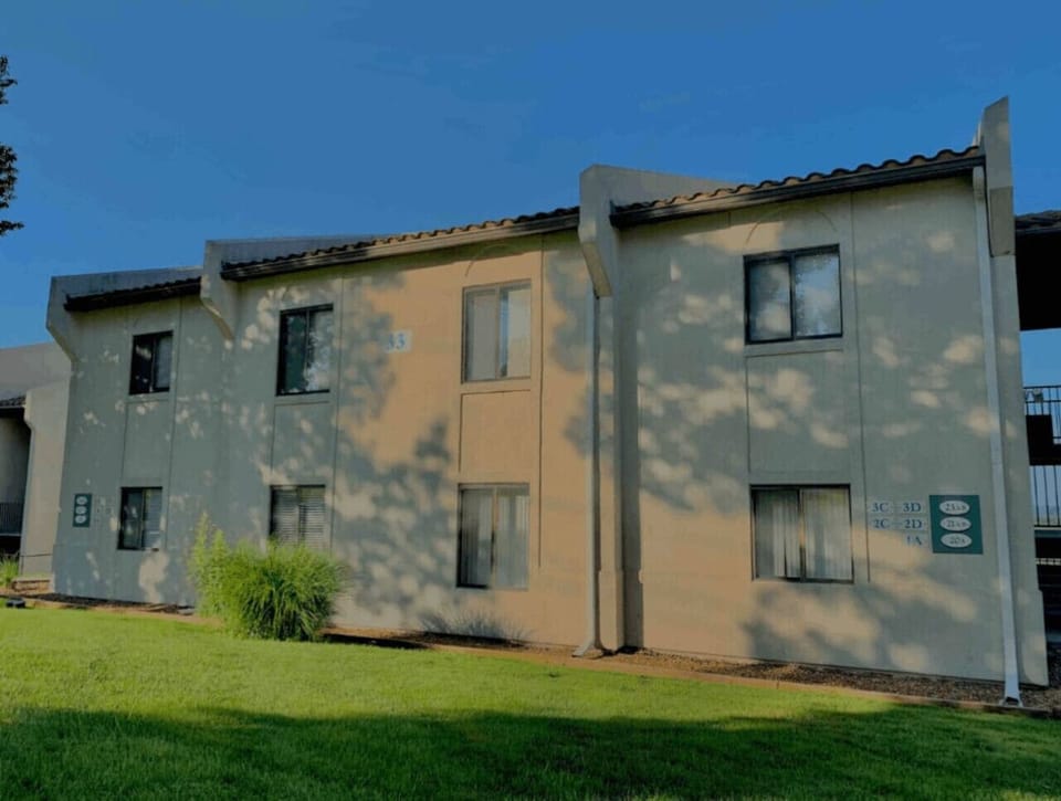 Your inviting retreat is located in this charming apartment building, featuring a tan exterior and nestled on a well-maintained grassy slope.