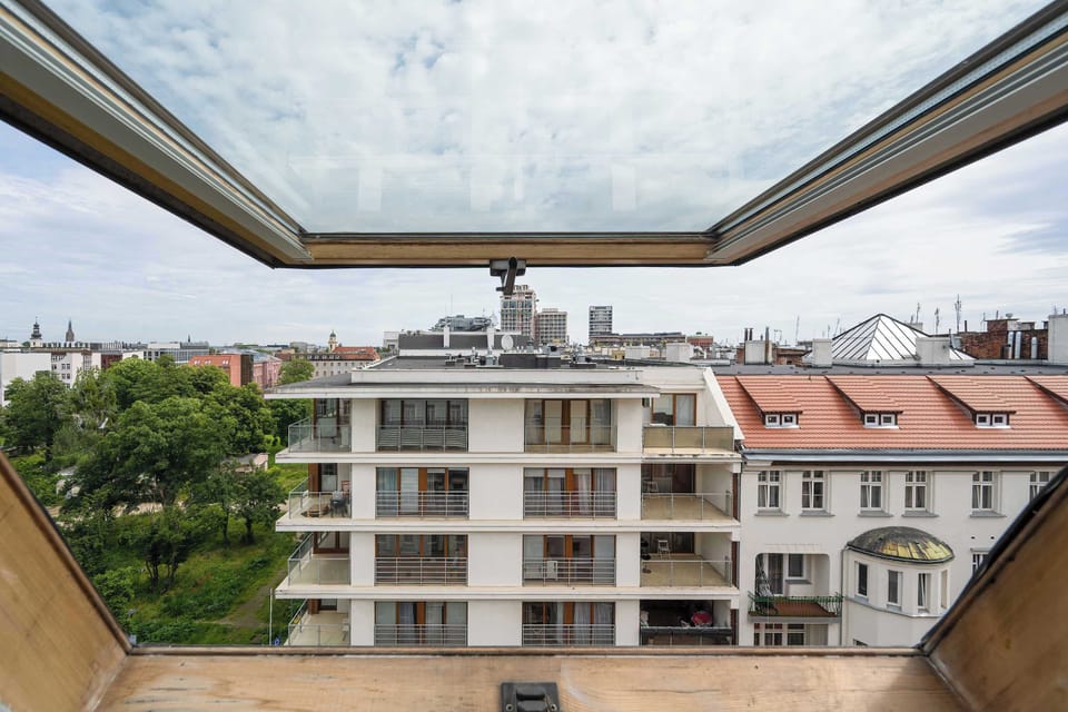 A view from the large window showcasing the rooftops and greenery of the surrounding buildings.