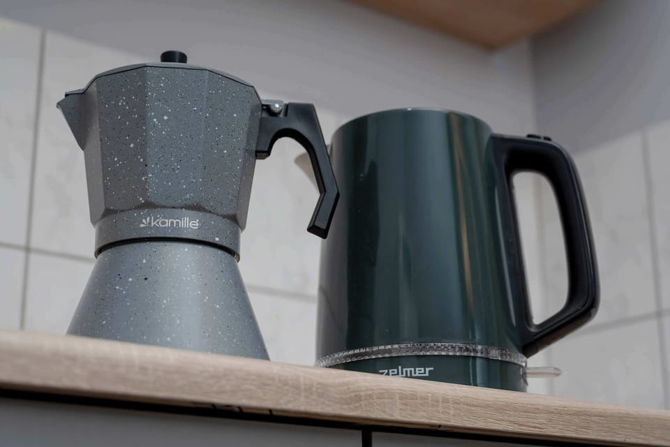 A close-up of a coffee corner with a moka pot and an electric kettle placed on a wooden counter.