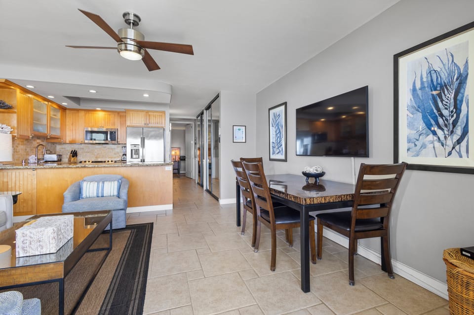 Relax in your open-concept living space where the fully-equipped kitchen flows into a cozy dining area. Enjoy meals together beneath coastal-inspired artwork and a modern ceiling fan keeping you comfortable.