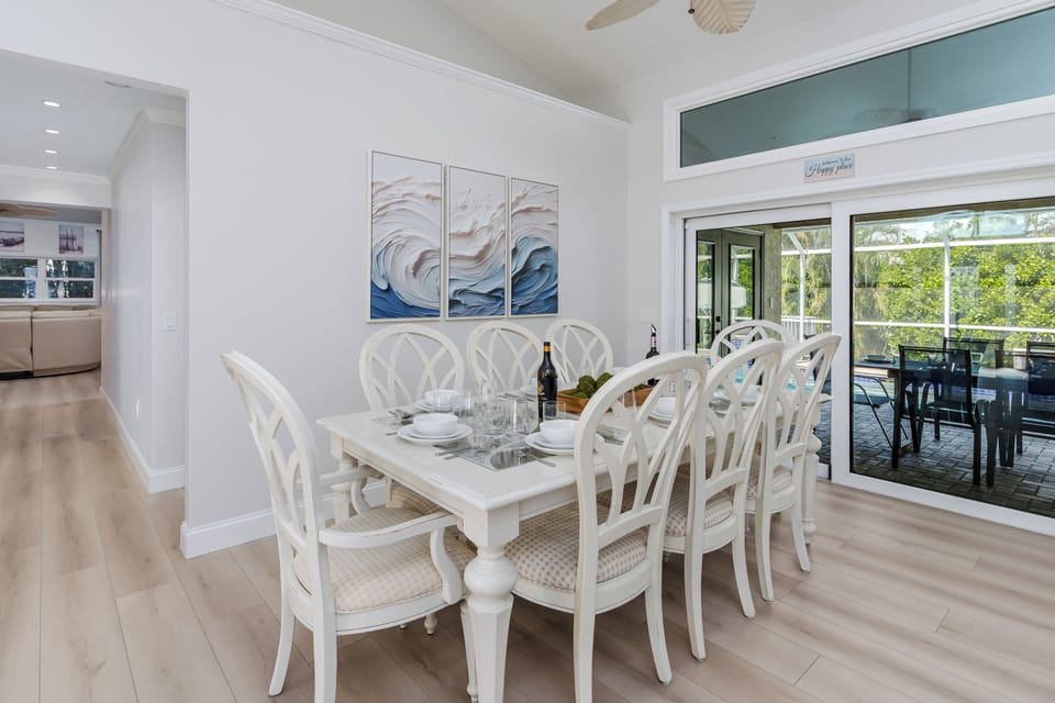 Gather around this elegant dining table where memorable meals unfold beneath coastal artwork. The space flows seamlessly from kitchen to outdoor terrace, creating the perfect atmosphere for your vacation dining experiences.
