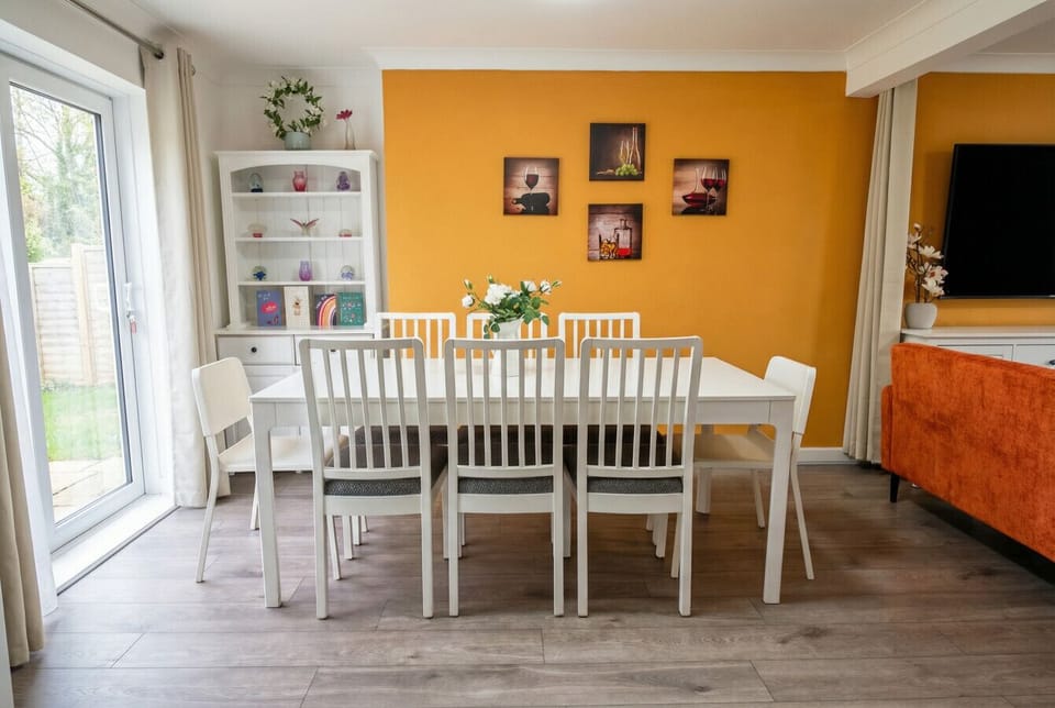 White dining table with mixed white chairs beside a glass-front cabinet and a glazed door with curtains.