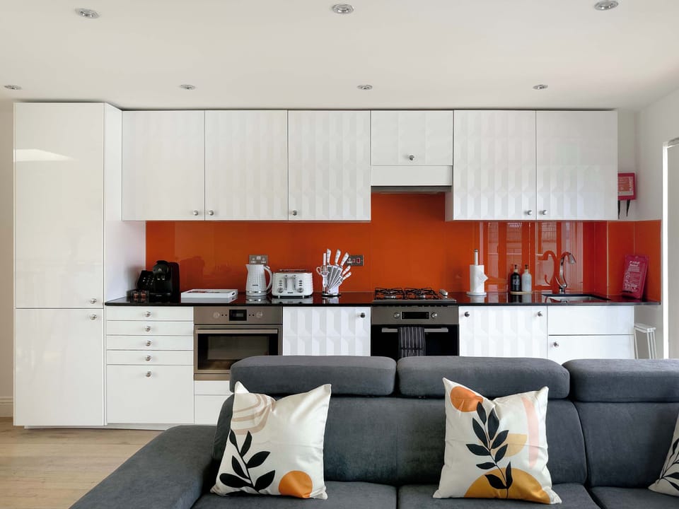 Sunlit open-plan living, kitchen and dining area with floor-to-ceiling windows, creating a bright, airy and welcoming space to relax and entertain