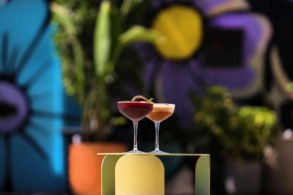 Two vibrant cocktails with bold floral wall backdrop