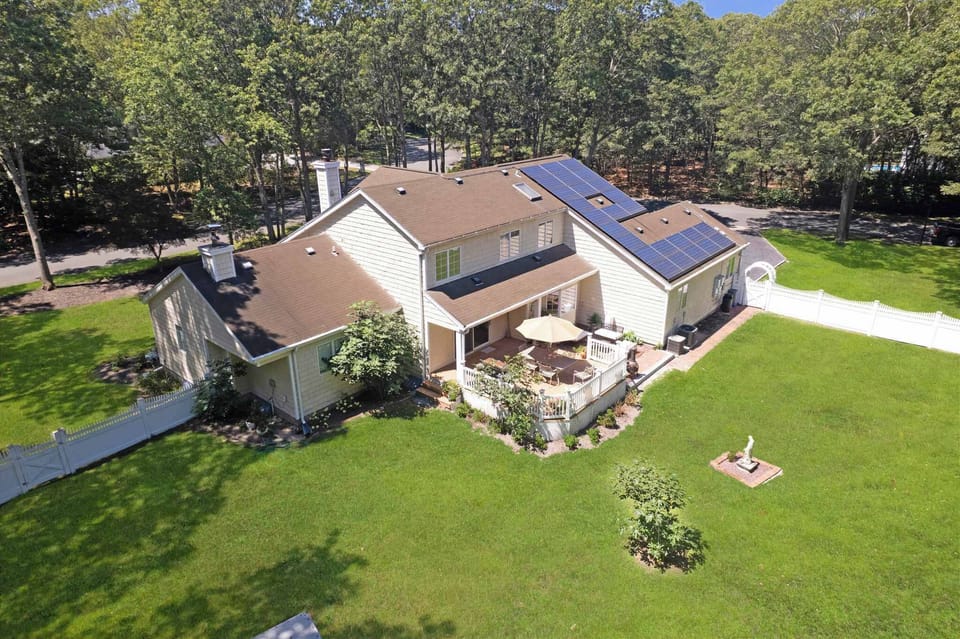 Aerial view of rear deck, fenced yard, and wooded lot