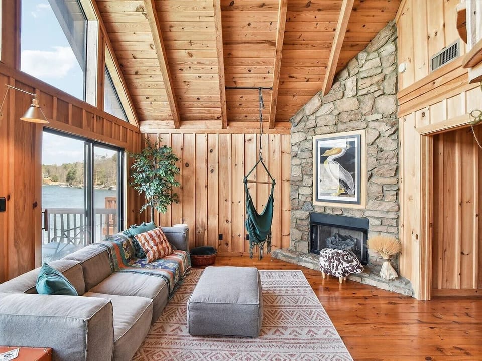 Step into the bright and airy living room of this stunning A-frame lakehouse chalet, where modern comfort meets cozy charm. A low, plush modern sofa invites you to relax beneath soaring vaulted ceilings, while a stylish green hanging chair adds a playful,