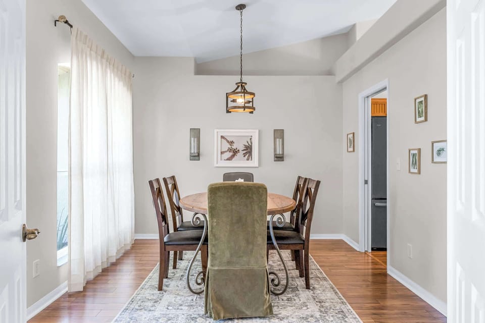 Dining area with a round wooden table, mixed seating, and natural light from sheer curtains.