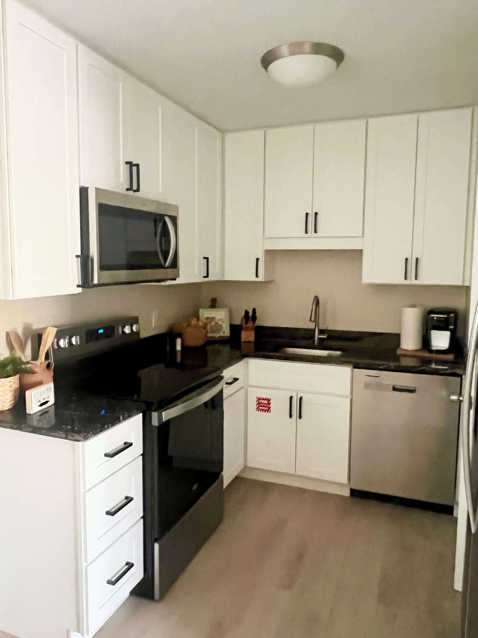 Modern kitchen with white cabinetry, stainless steel appliances, and black countertops.