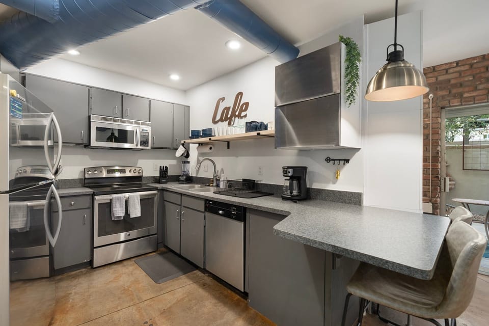 This kitchen features stainless appliances, open counters, and industrial touches paired with warm brick accents. Set up at the island, prep meals with room to move, and enjoy the mix of modern finishes and practical layout for everyday cooking.