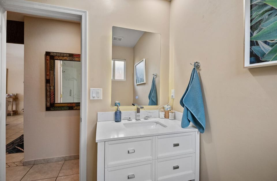 Freshen up with ease at the bathroom vanity featuring a well-lit mirror, sink, and thoughtfully stocked essentials like cotton buds, tampons, and more.