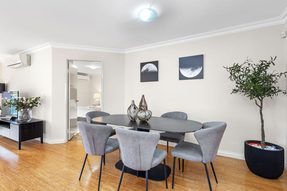 Dine in a chic space featuring a dark oval table and grey chairs, complemented by artistic wall decor and elegant vases, offering a refined dining experience.