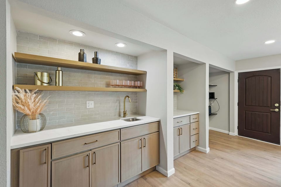 Stylish wet bar with open shelving, modern decor, and a sleek gold faucet. 

