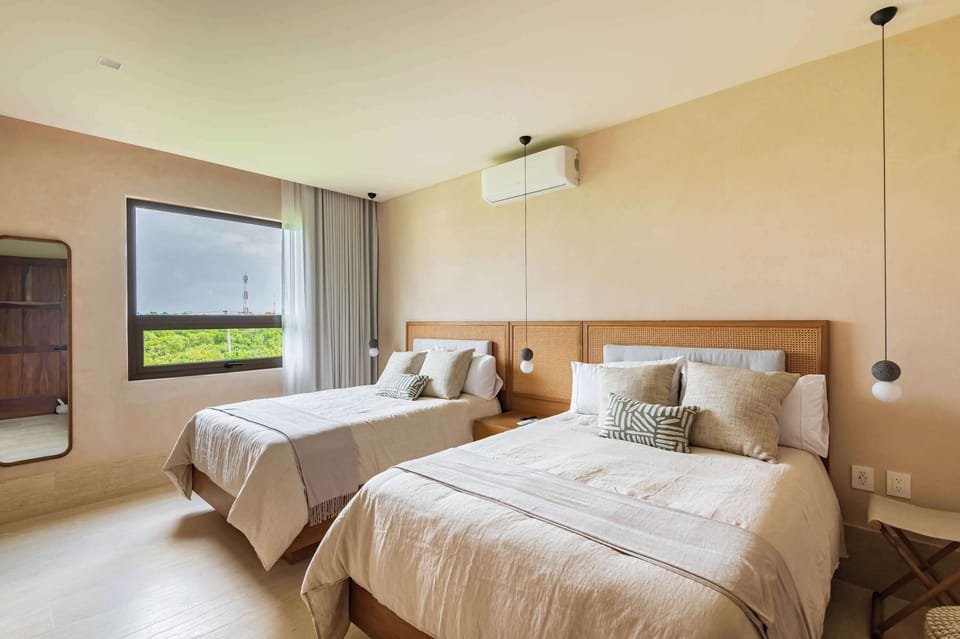 The room features neutral-toned walls and light-colored flooring, creating a calm and airy atmosphere.  The two twin beds are neatly made with light grey bedding and decorative pillows.