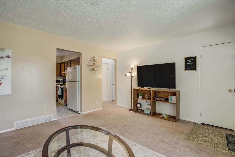 The living room includes a large Smart TV and open shelving for games and essentials, with easy access to the kitchen and hallway for a functional flow.

