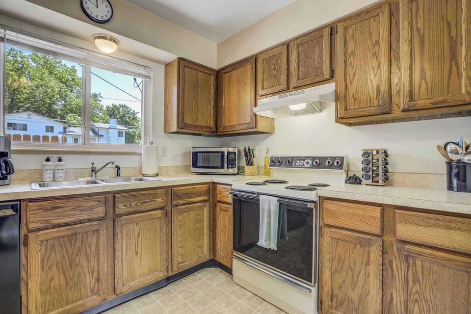 The fully equipped kitchen features classic wood cabinetry, an electric range, microwave, coffee maker, and a window over the sink with views of the backyard.


