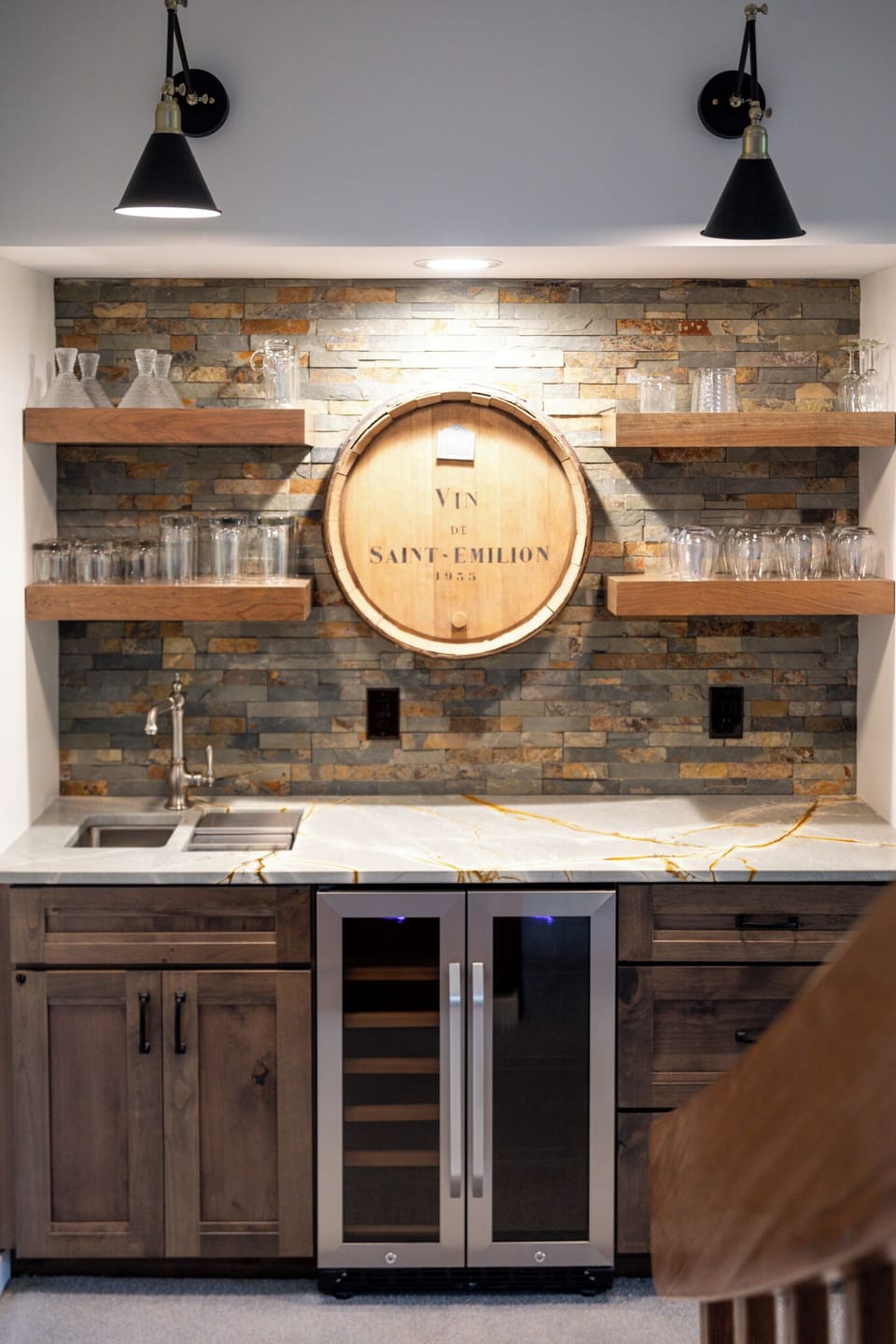Stylish basement bar with a wine fridge, stone backsplash, and open shelving—ideal for casual entertaining or an evening drink.